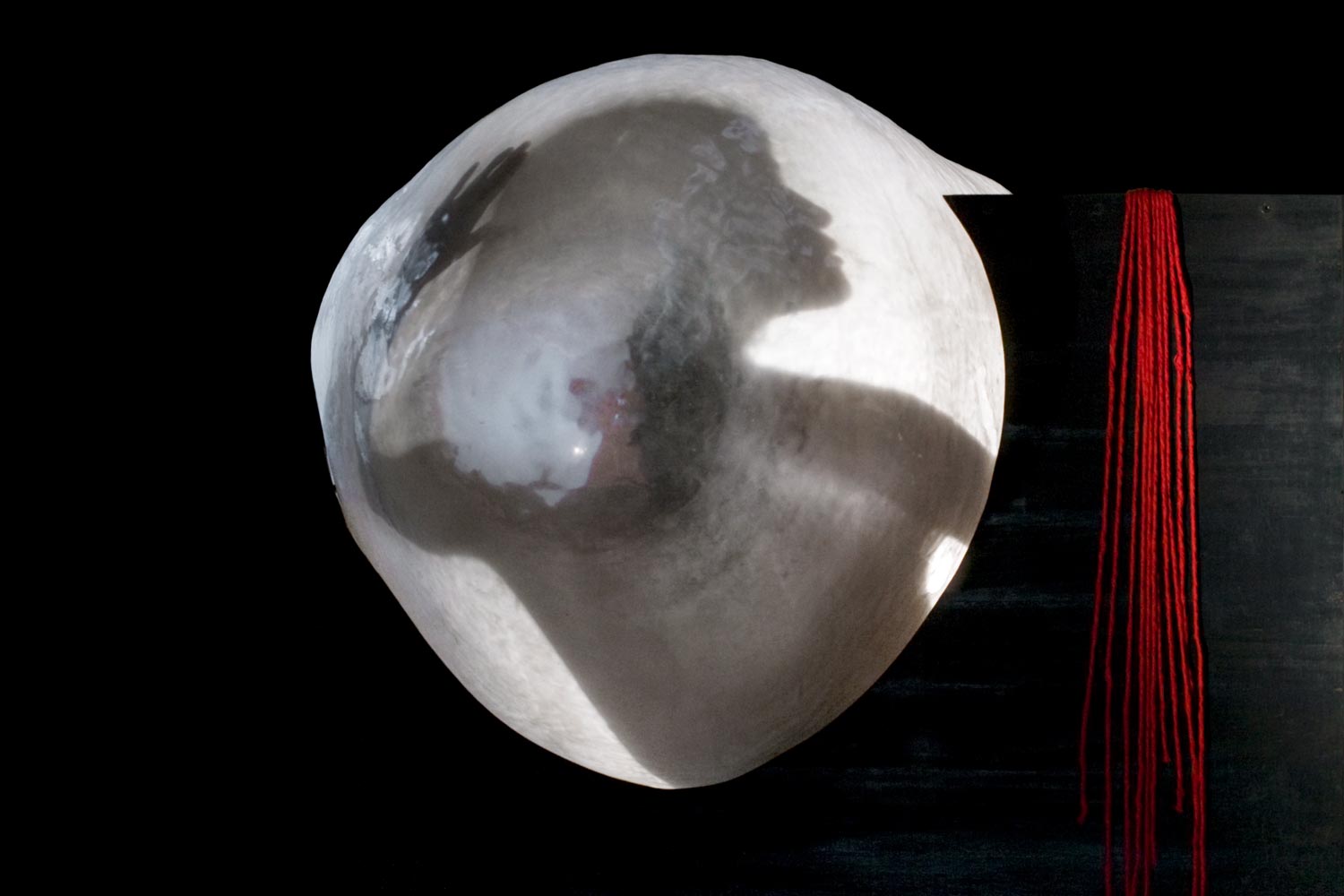 A translucent sleeping figure emerging from a black box draped with red thread