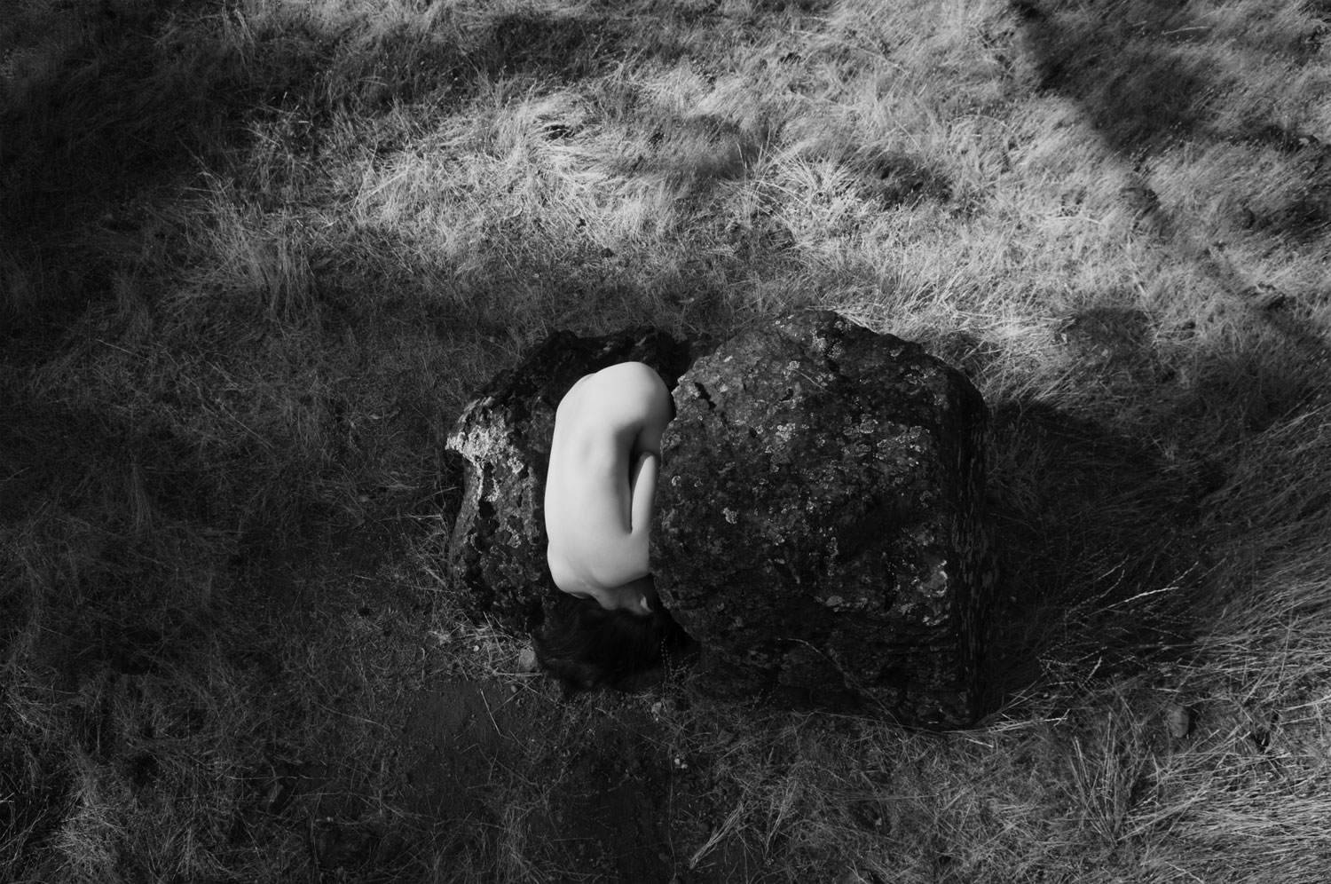 A dancer curls into the opening of a broken rock, seen from above