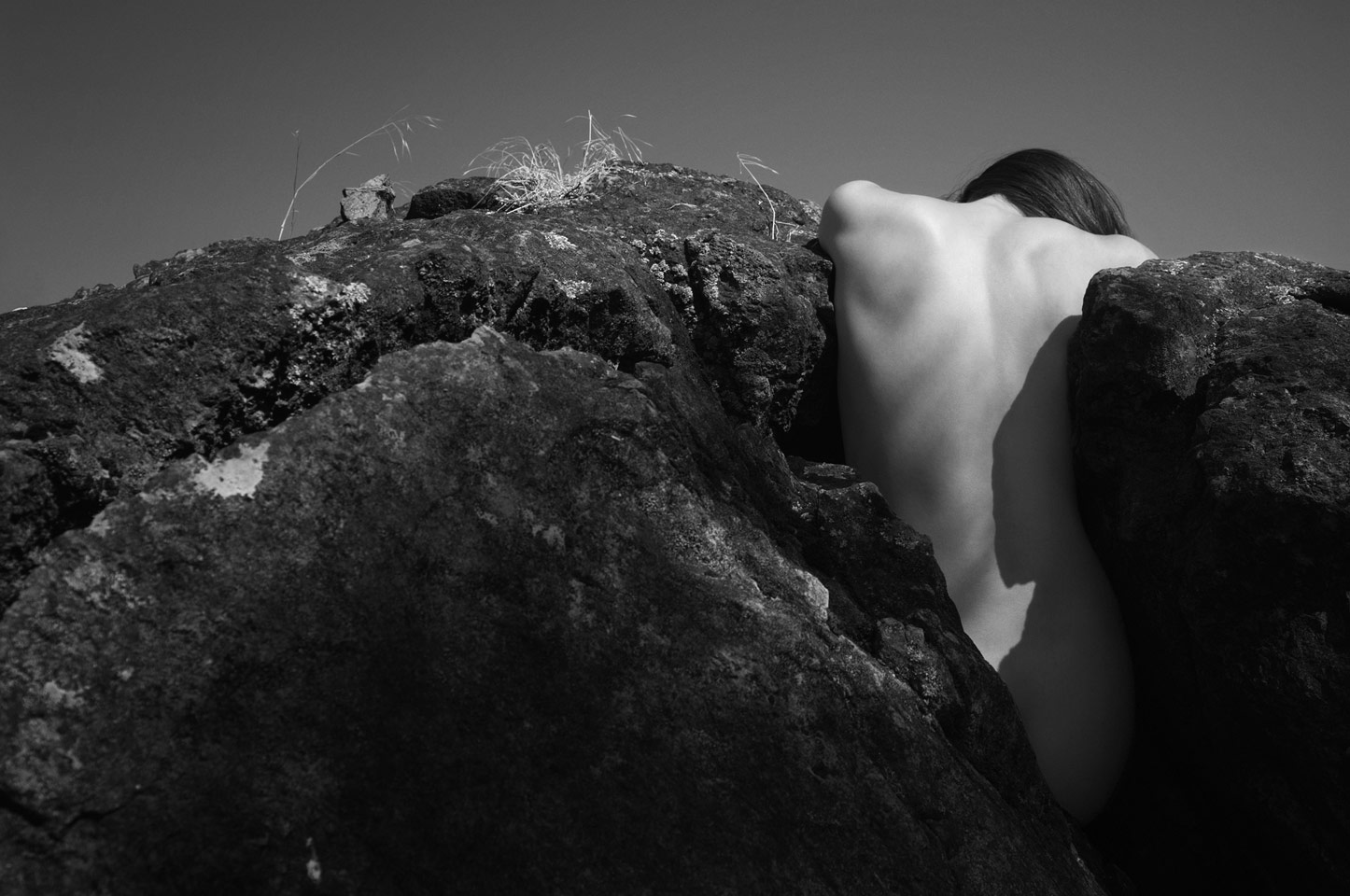 A dancer's back emerges from a deep split in a rock