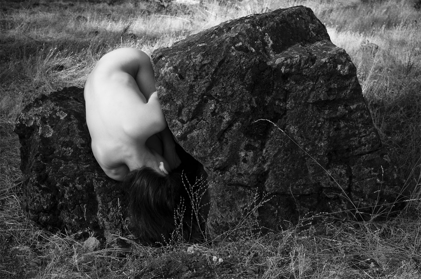 A curled dancer fits closely into the hollow of a broken rock